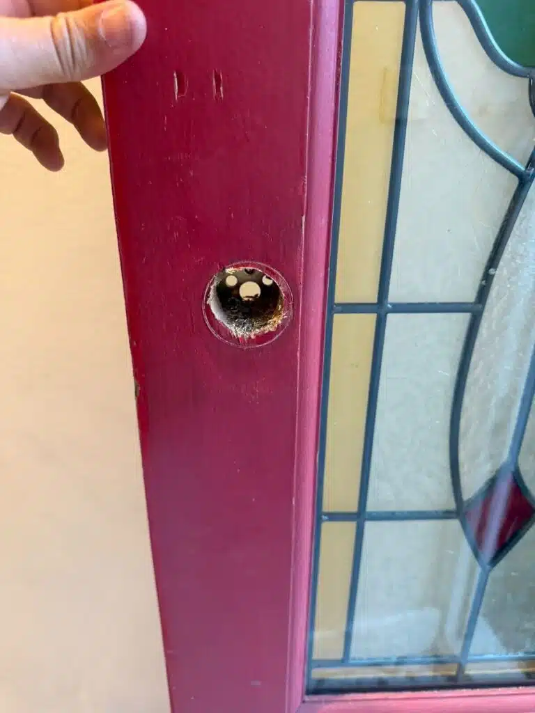 Damaged door lock hole on red front door requiring repair